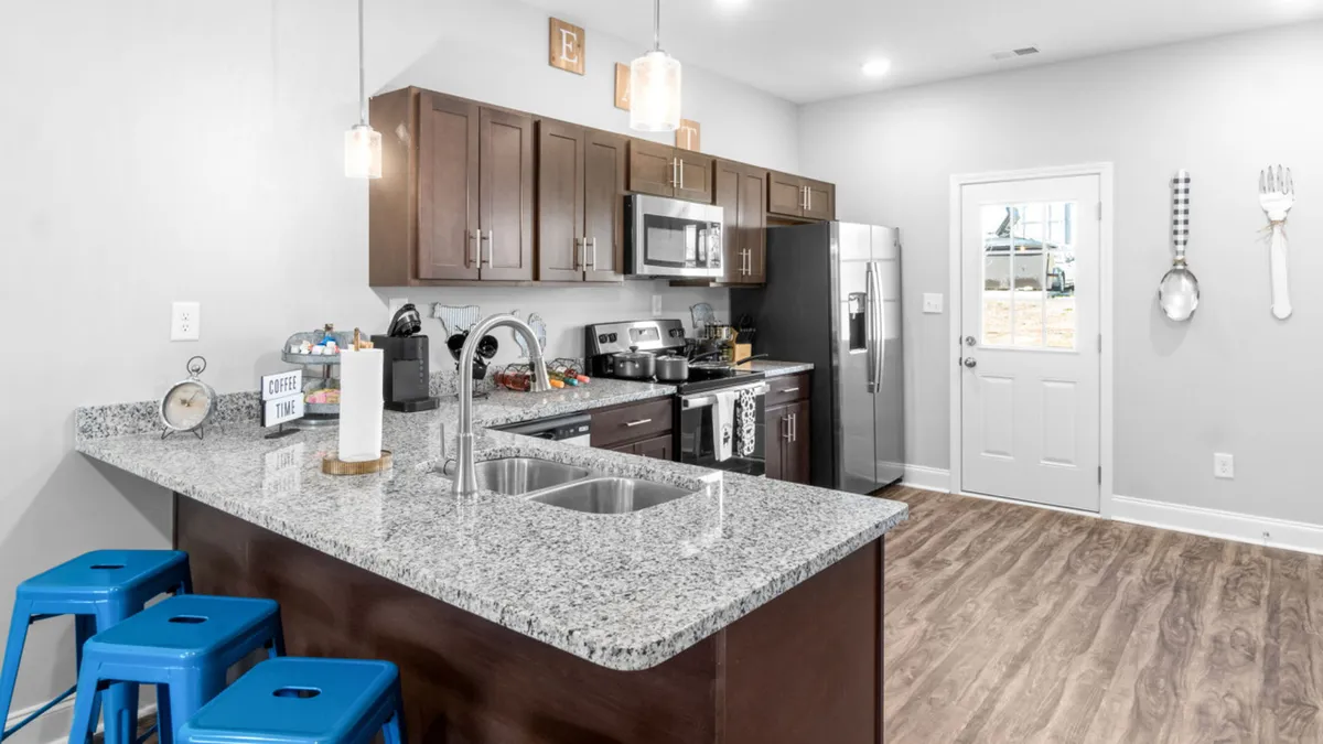 A modern kitchen highlighted by granite countertops, stainless steel appliances, blue stools, and bright cabinetry. The space invites meal preparation, morning coffee rituals, and intimate family moments.