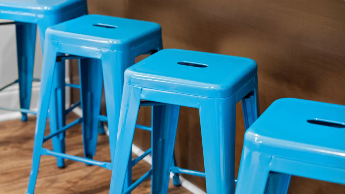 A casual dining space highlighted by bright blue stools and a wooden accent wall. The seating arrangement is ideal for casual dining, brunches, or relaxed conversations among friends.
