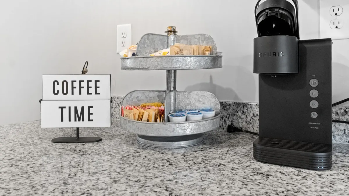 A cozy coffee station is featured, complete with a coffee maker, a welcoming 'Coffee' sign, and an organized condiment holder. The setup evokes shared morning rituals and relaxed beginnings to the day, ideal for couples seeking a gentle start to their getaway.