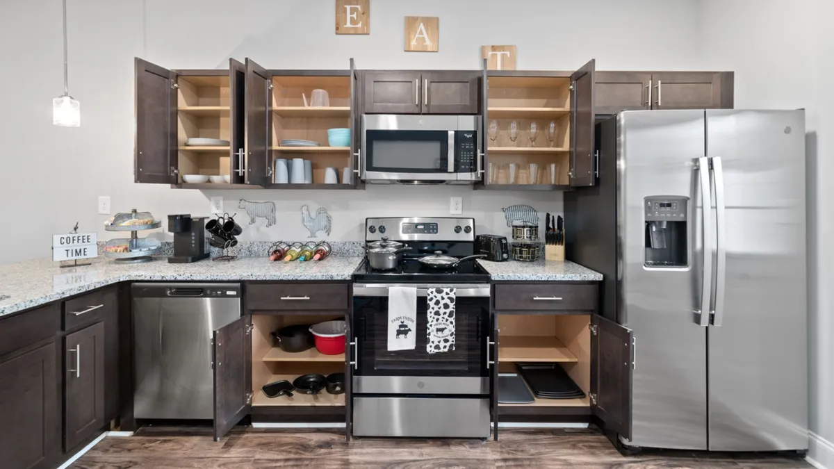 A stylish kitchen featuring stainless steel appliances, a granite countertop, open shelving, and a coffee sign. The environment is warm and functional, ideal for preparing meals or sharing a celebratory toast with friends.