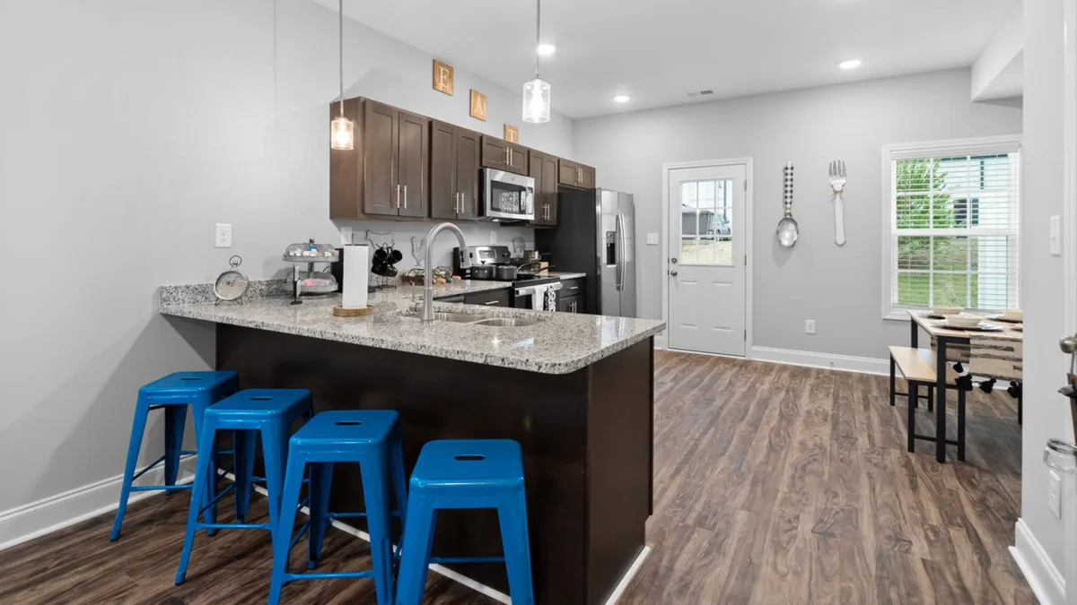 A striking modern kitchen with a granite countertop, blue bar stools, and stainless steel appliances. The scene exudes a contemporary aesthetic, with ample seating for casual dining or lively conversation during meal prep.