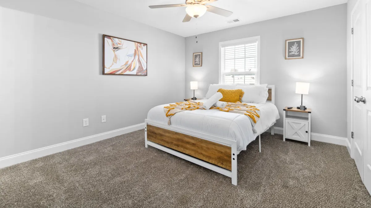 A master bedroom featuring a plush bed with a decorative throw, artwork adorning the wall, and nightstands with warm, glowing lamps. The overall atmosphere is cozy, inviting, and designed for comfort, ideal for relaxation after a long day.