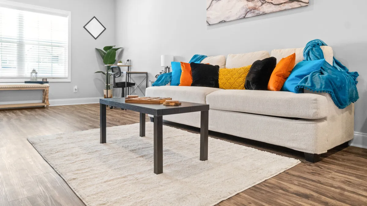 A comfortable living area with a plush sofa, coffee table, decorative pillows, and art on the wall. The space is inviting for relaxation, socializing, or unwinding after a long day of work.