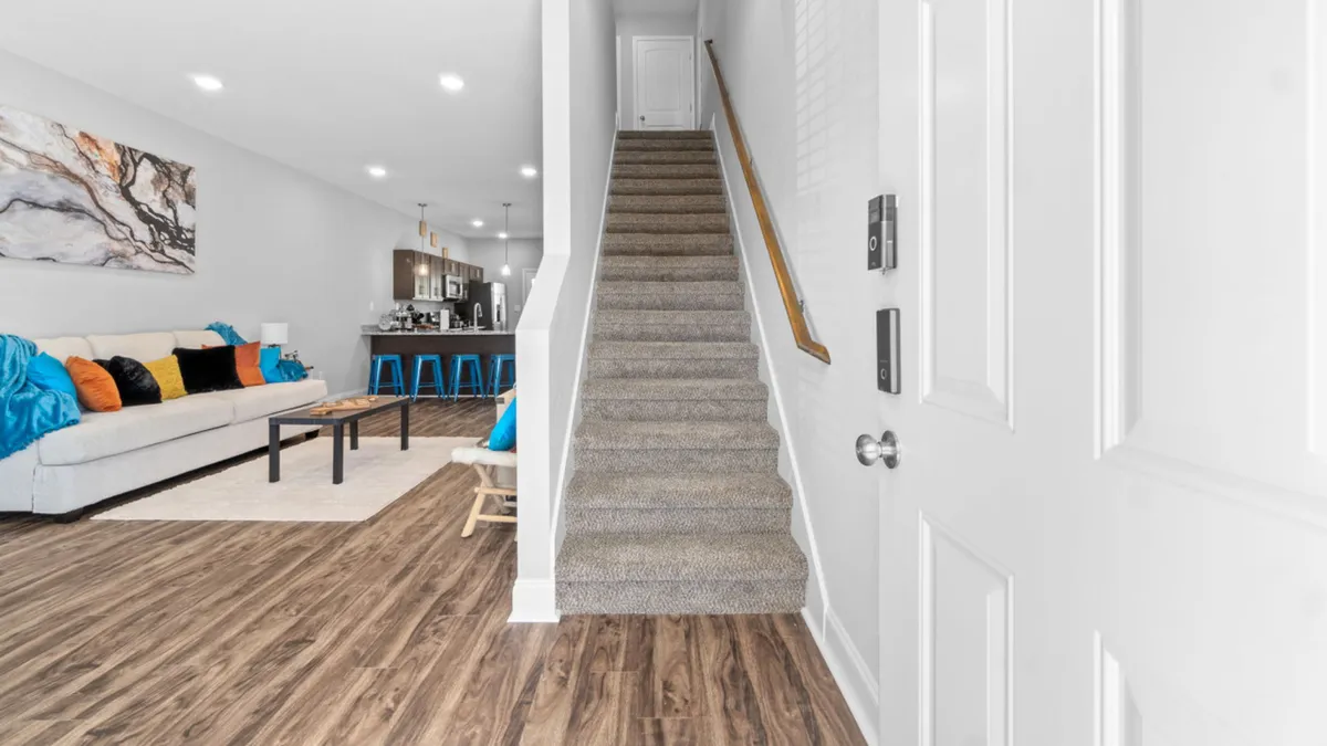 A contemporary, open-plan living space with a cozy sofa adorned with colorful cushions, a staircase leading to upper levels, a stylish bar area with stools, and vibrant artwork on the wall. The room exudes a family-friendly, relaxing vibe.