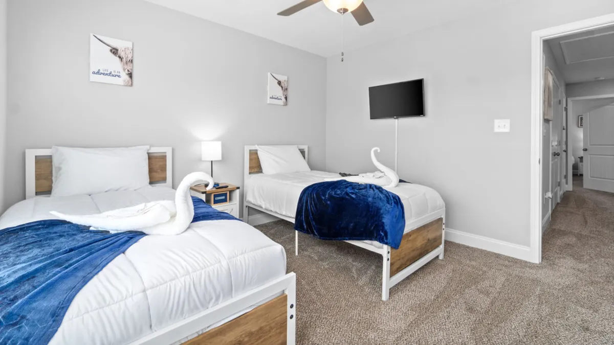 A secondary bedroom showcasing two twin beds with towel swan decorations, blue throw blankets, and wall art that adds a cheerful touch. The space is bright and inviting, perfect for guests or family members seeking their own cozy retreat.