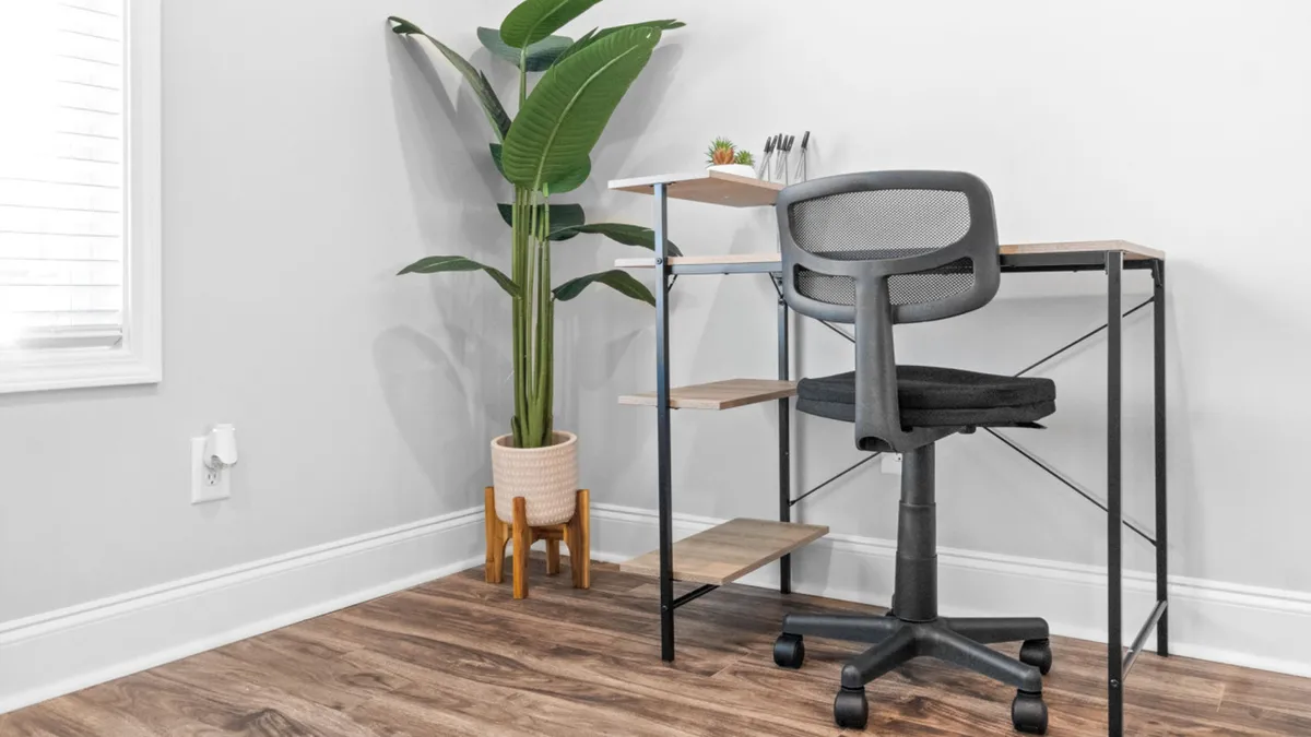 A calm and focused workspace featuring a well-organized desk with a comfortable chair and a potted plant nearby. Natural light enhances the setting, making it ideal for productivity and remote work.